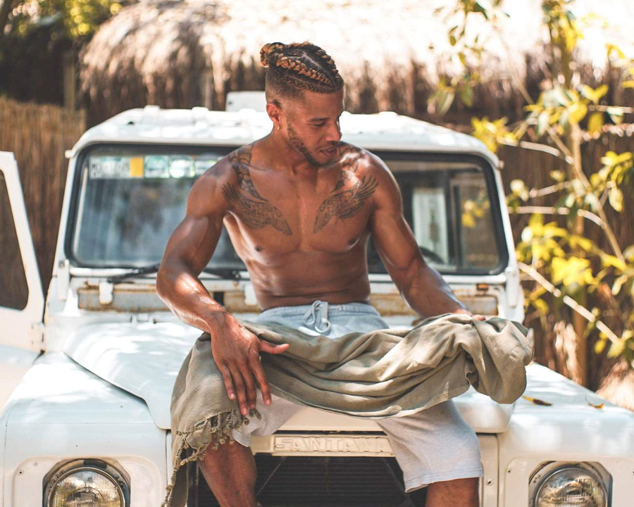 tattooed man sitting on a Land River holding a beach towel