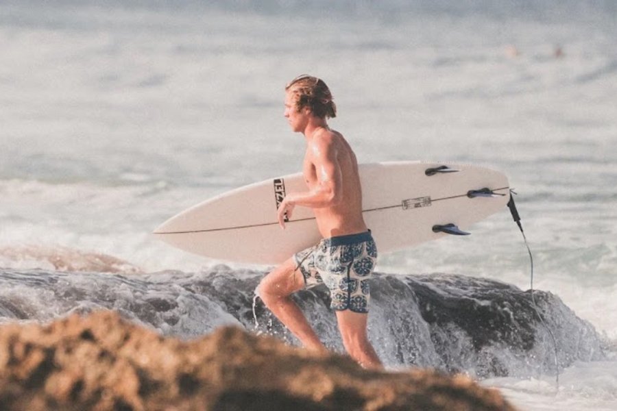 man in surf trunks carrying a surfboard