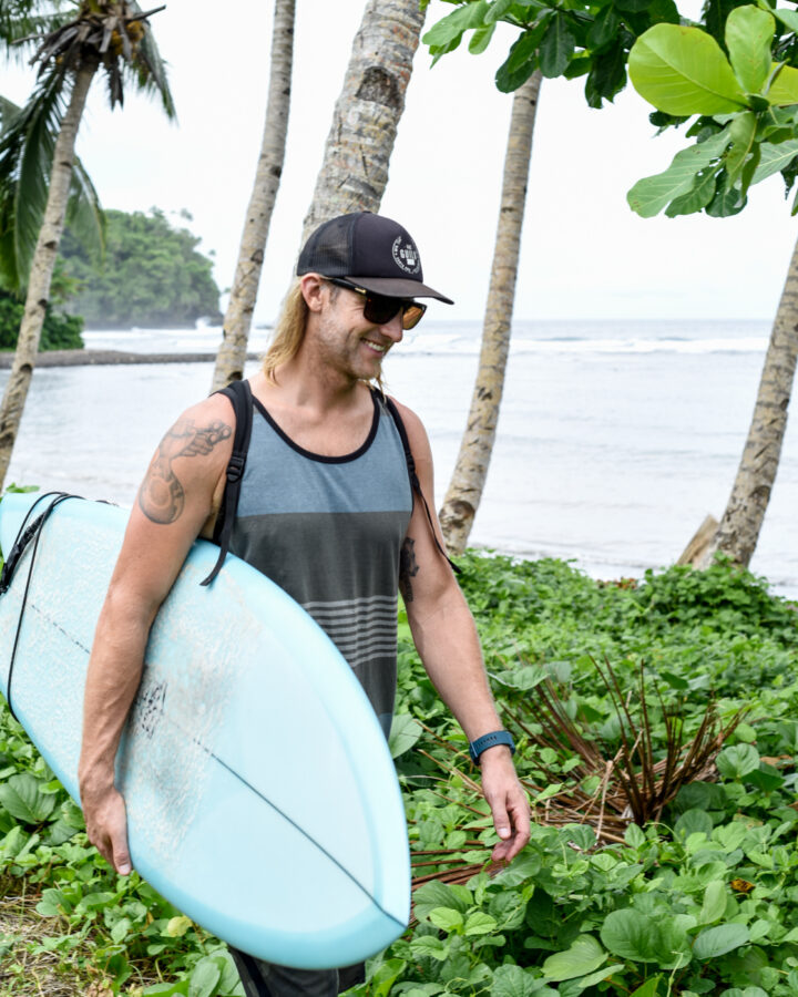 co-founder Eric walking on tropical beach with surfboard