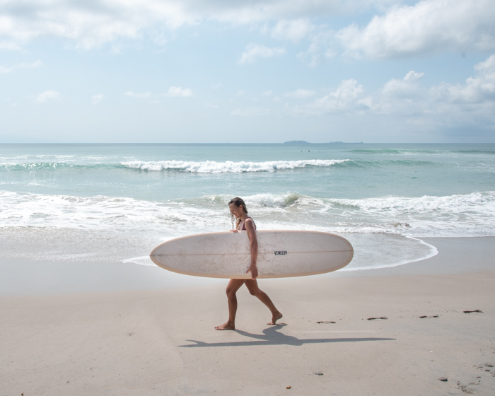 girl holding surfboard walking on beach