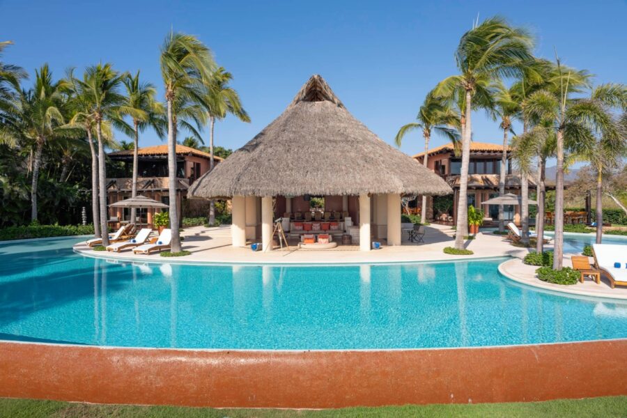 large infinity pool surrounding a thatched-roof lounge area with palm trees