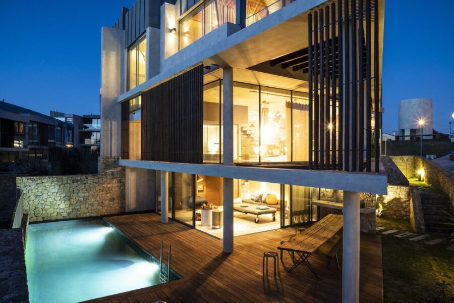 modern luxury villa at night with large glass windows, private pool, and wooden deck.
