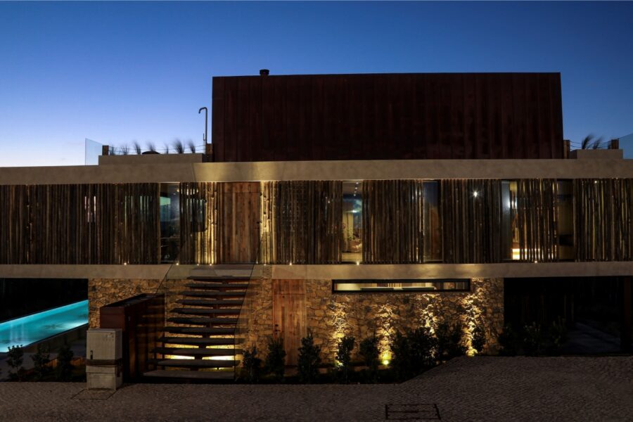 modern villa at dusk with stone accents, wooden slats, and illuminated exterior lighting