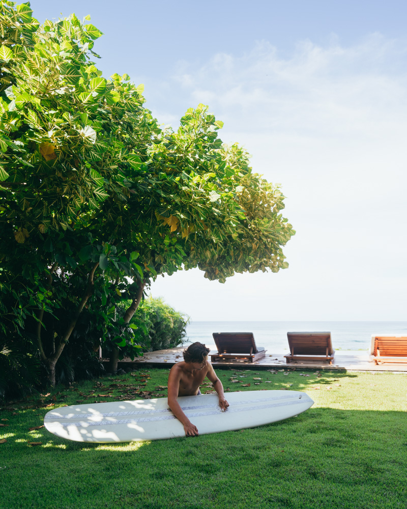 guy waxing surfboard in shady grass