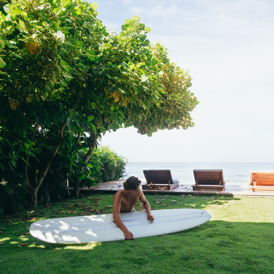 guy waxing longboard surfboard by in grass by pool