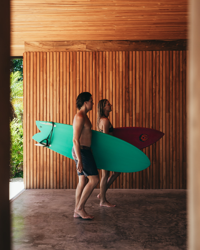 guy and girl carrying surfboards through villa