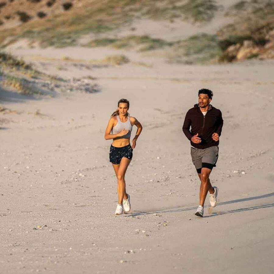man and woman jogging on beach - wearing california surf brand Vuori