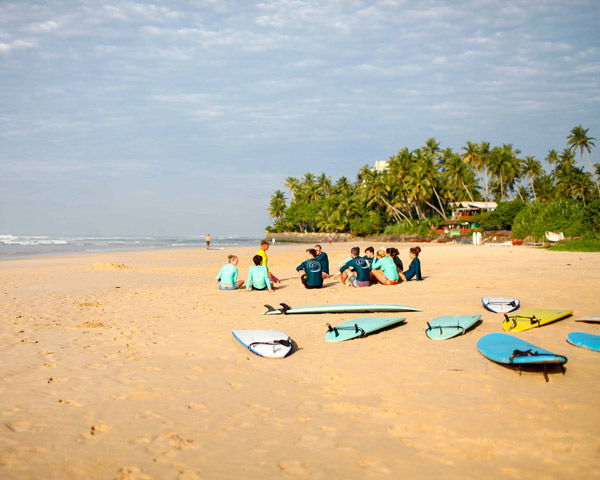 surfers sitting on beach around surf instructor