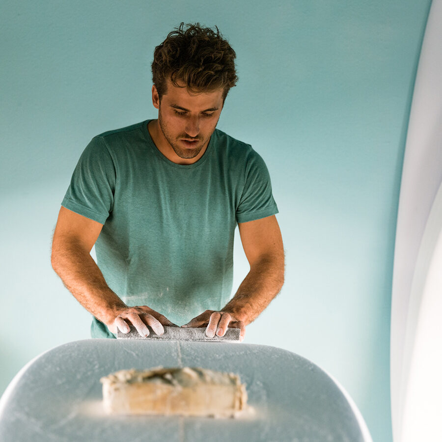 man shaping surfboard wearing hemp t-shirt by wellen