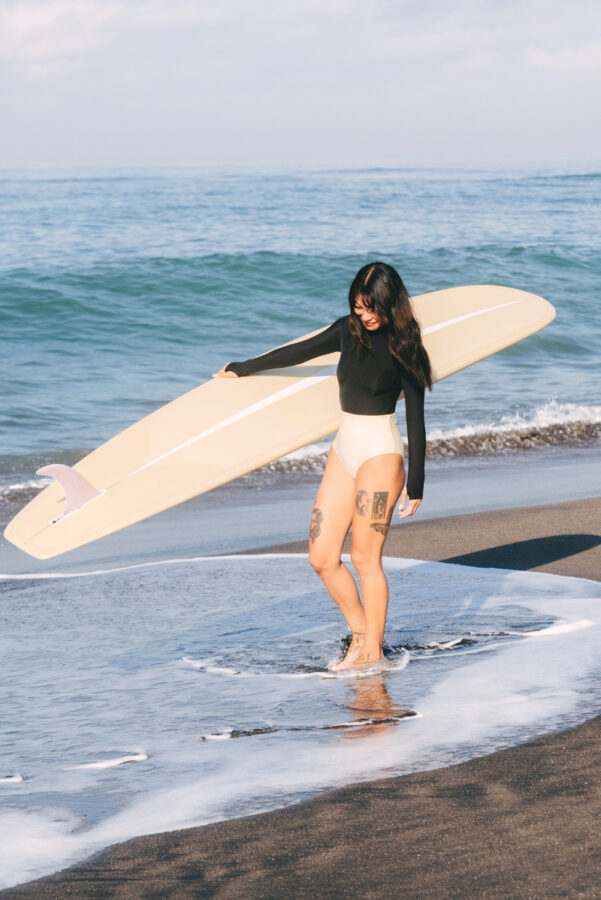 girl holding surfboard / sustainable swimwear for surfing